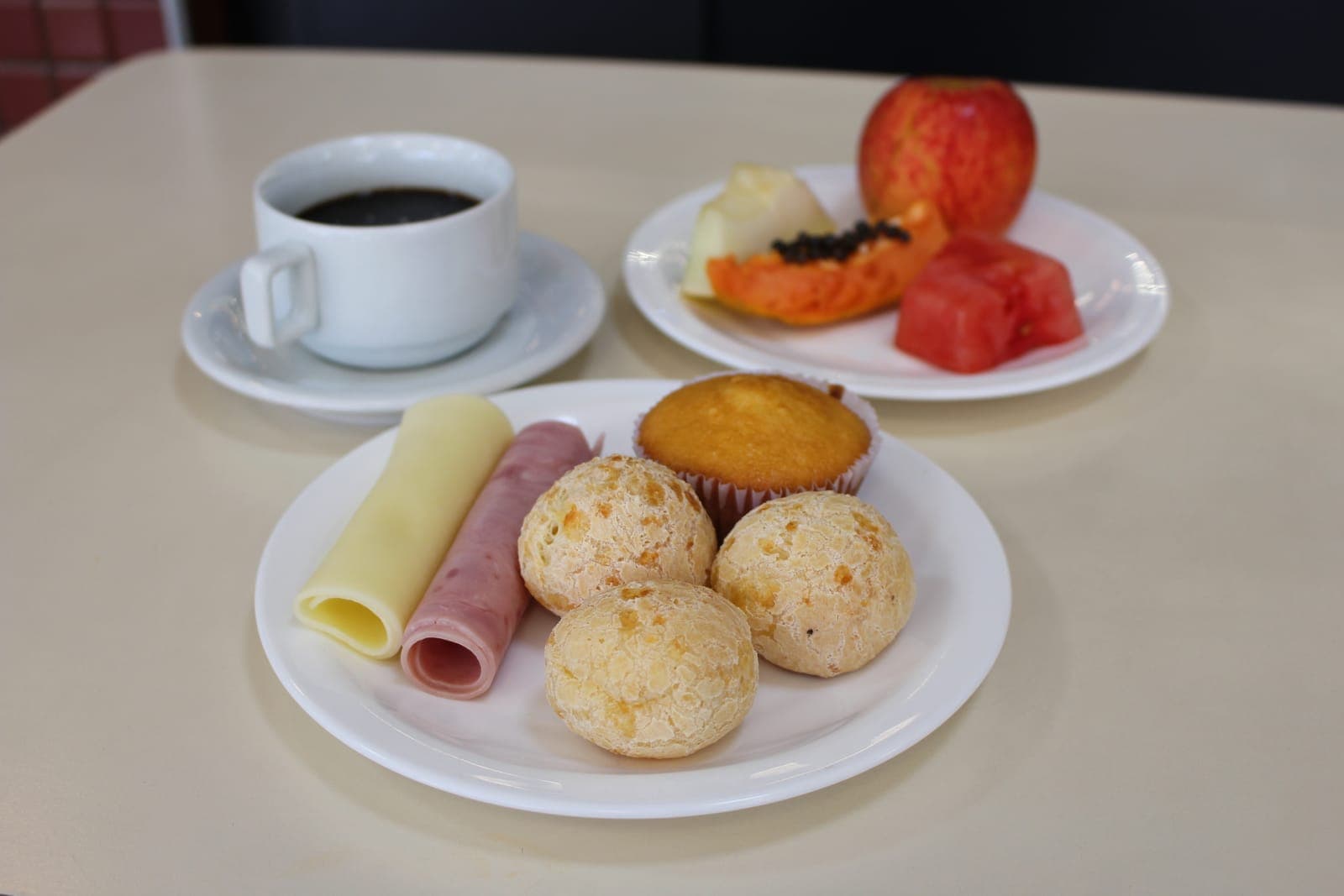 Café da manhã servido com pão de queijo, frios e frutas